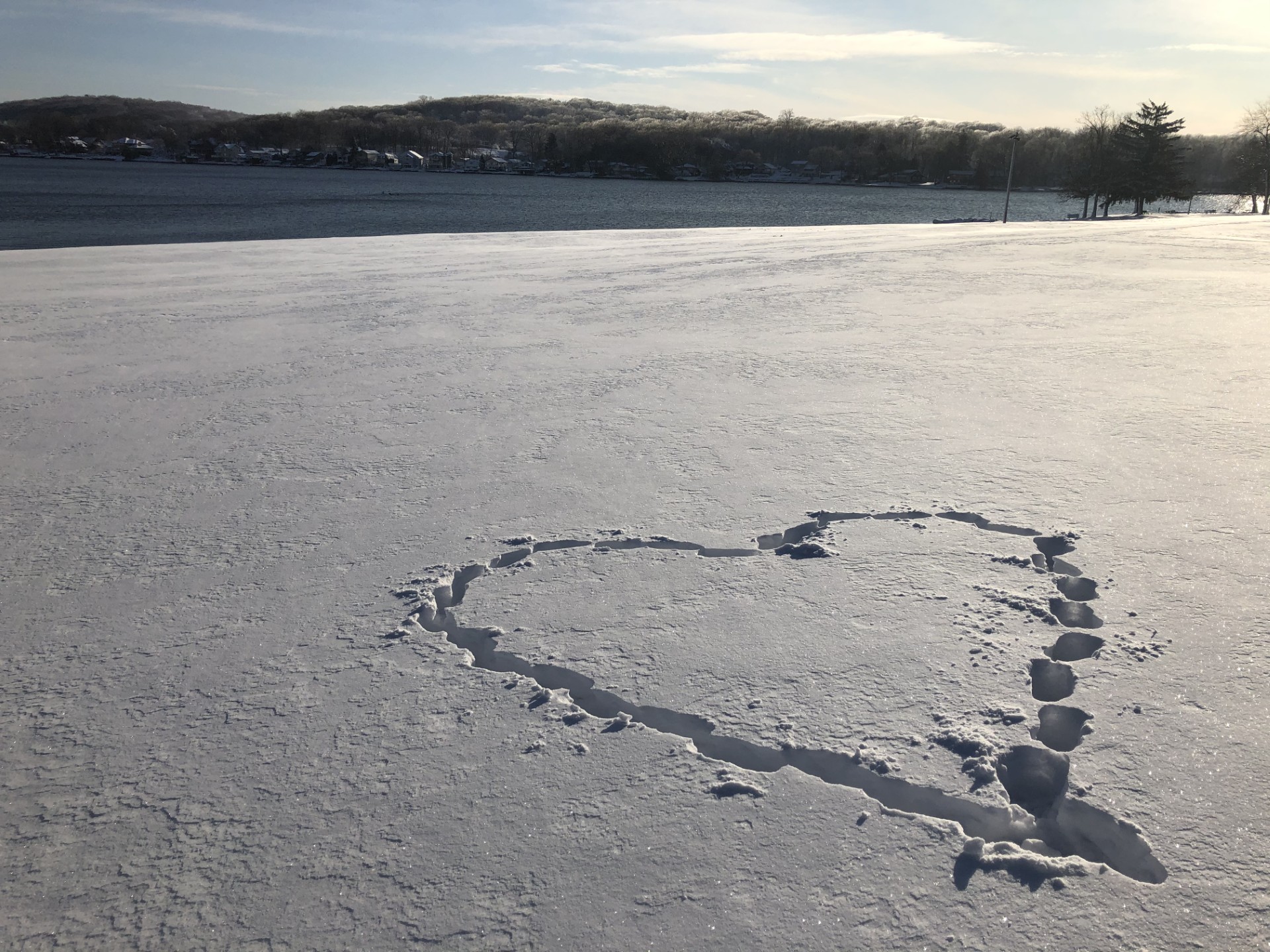 A heart, formed by footprints, made in a snowy landscape, lays beneath a frosty winter sky.