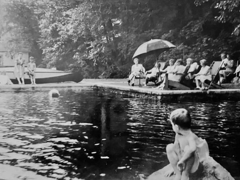 People sit on a dock on Lake Hopatcong.  Trees in the background.